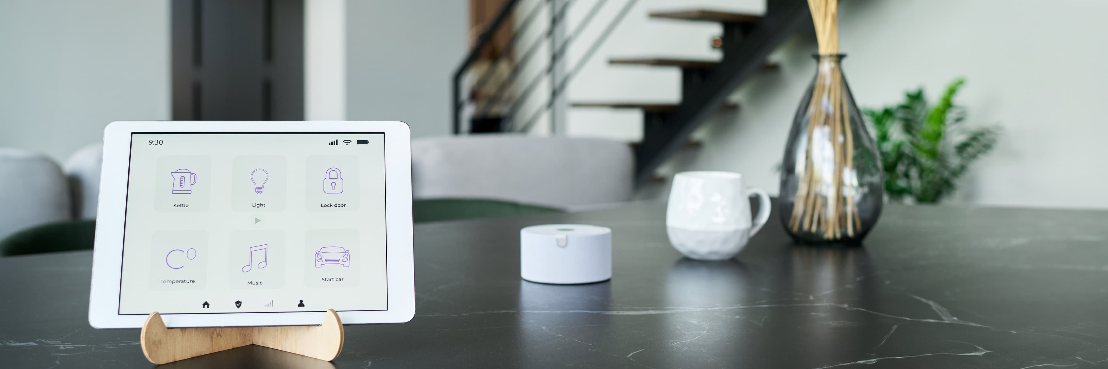 Tablet con interfaccia smart home su tavolo, accanto a tazza e diffusore.